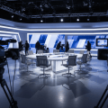 Studio de télévision abstrait, silhouettes floues autour d’une table de débat, éclairage froid bleu-gris, sans visage identifiable